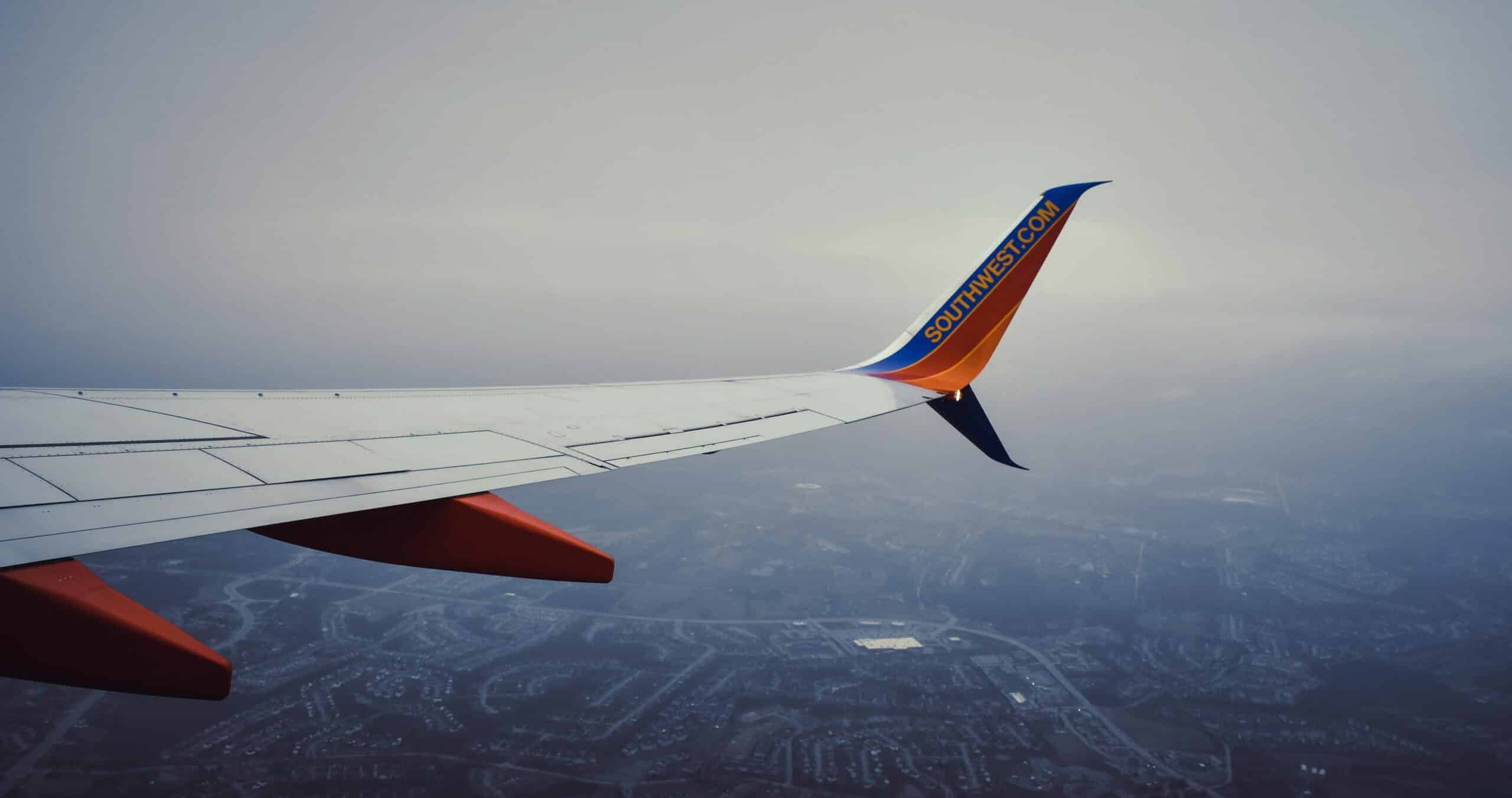 View of an airplane wing flying over a cityscape through a cloudy sky, offering a travel perspective.